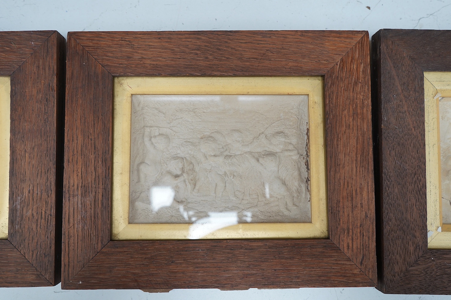 Three plaster relief panels depicting putti, framed, 21 x 25cm. Condition - two fair, one damaged